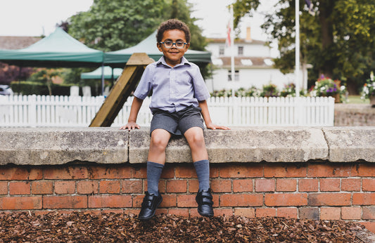 Kid wearing barefoot school shoes sitting on wall looking happy