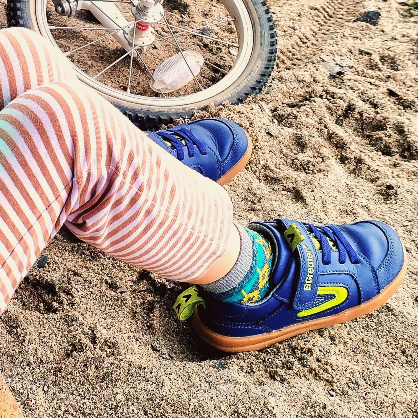Child's feet wearing blue sneakers with green accents on a sandy surface.