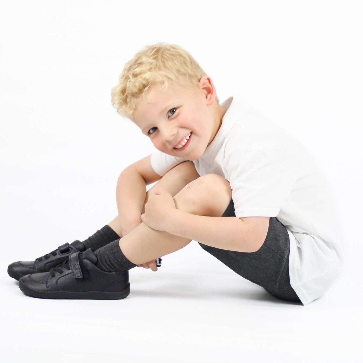 Child wearing black shoes and socks sitting on a white background