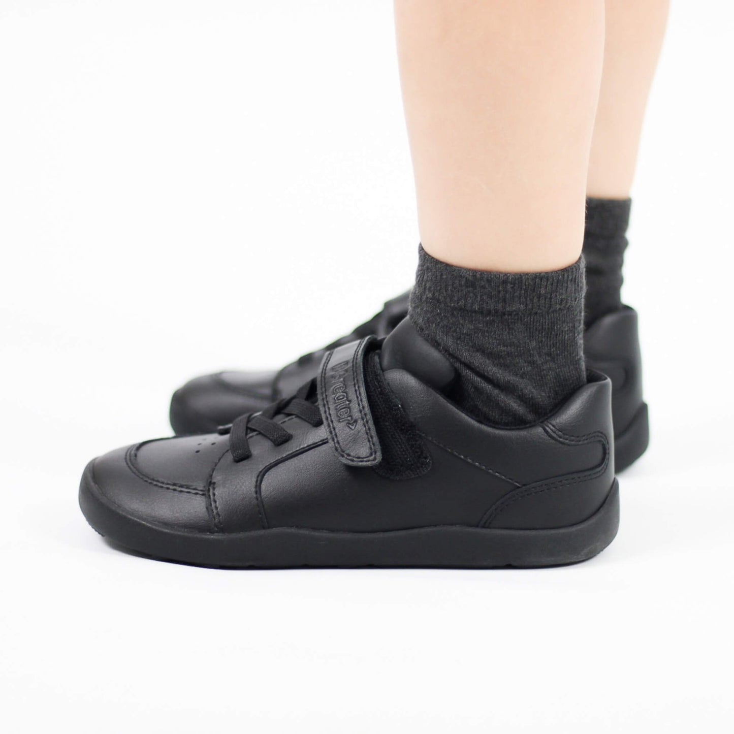 Black sneakers with velcro straps worn by a boy on a white background