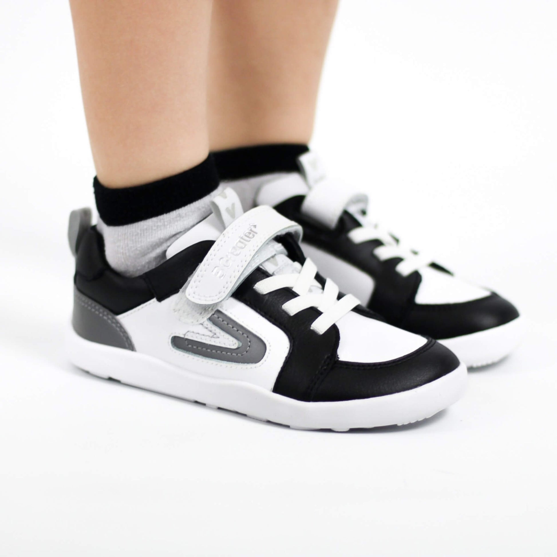 Black and white barefoot trainers worn with grey socks on a white background
