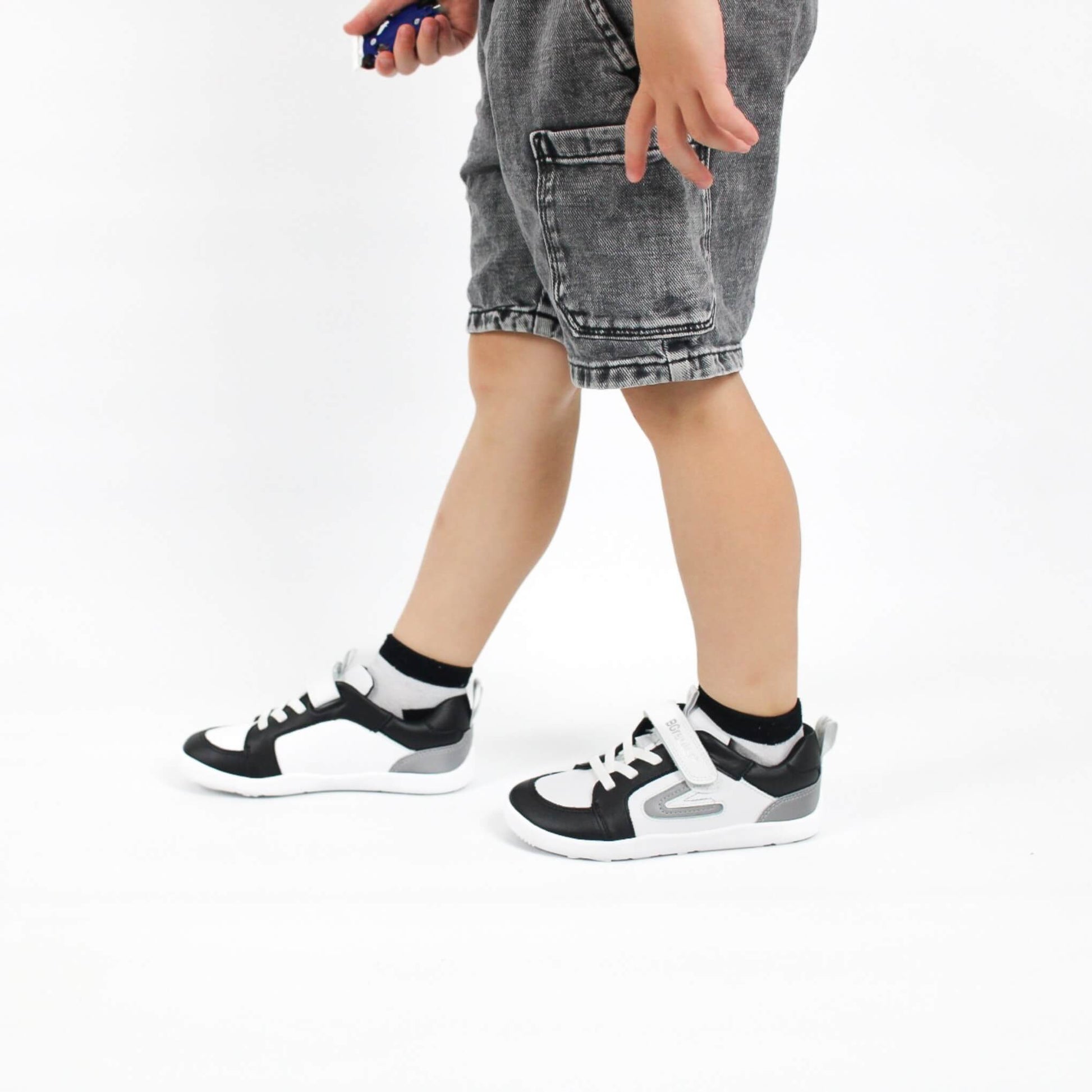 Boy wearing black and white barefoot trainers with grey shorts on a white background