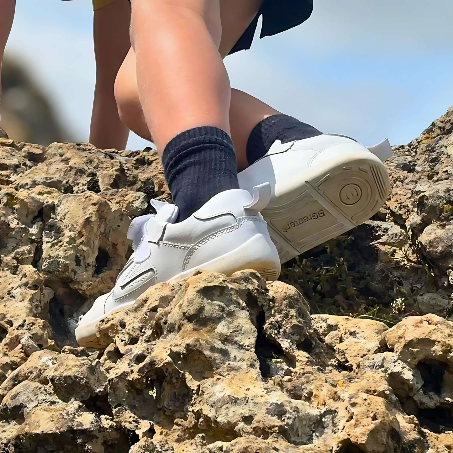 Boy is wearing white trainers and dark socks on rocky terrain