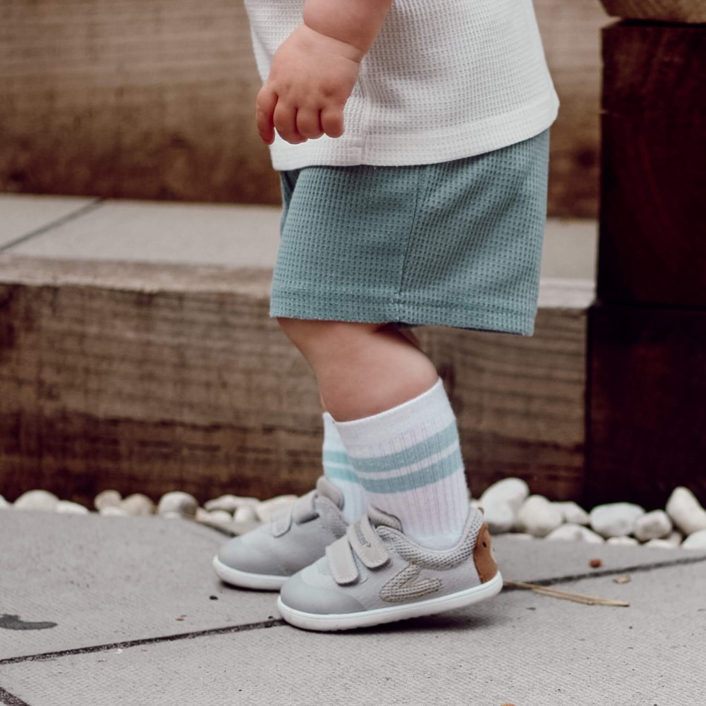 Side view of a kid wearing grey barefoot trainers outdoors on a stone patio.
