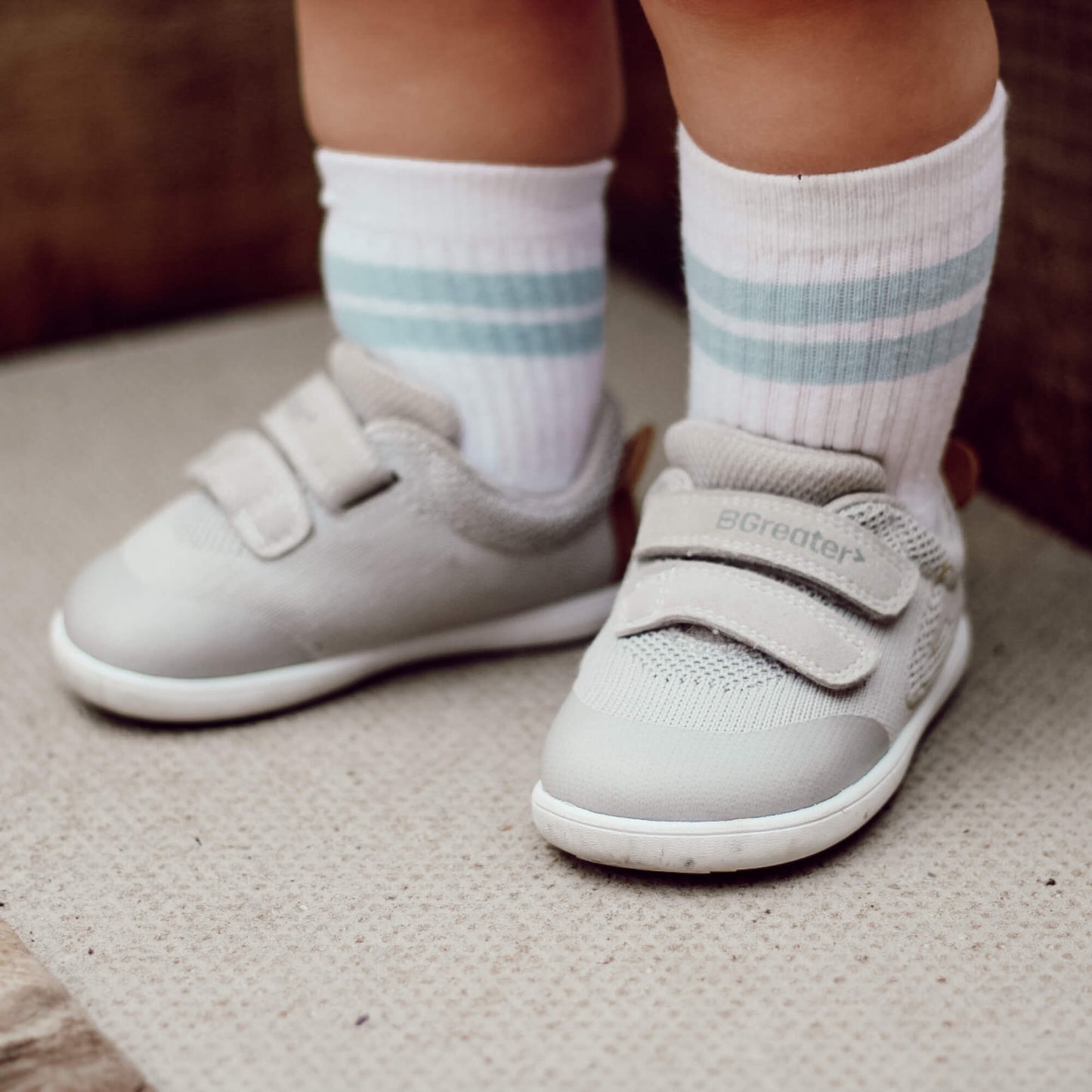 Kid's grey barefoot trainers with hook-and-loop straps pictured outdoors.