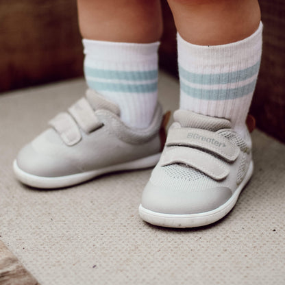 Kid's grey barefoot trainers with hook-and-loop straps pictured outdoors.