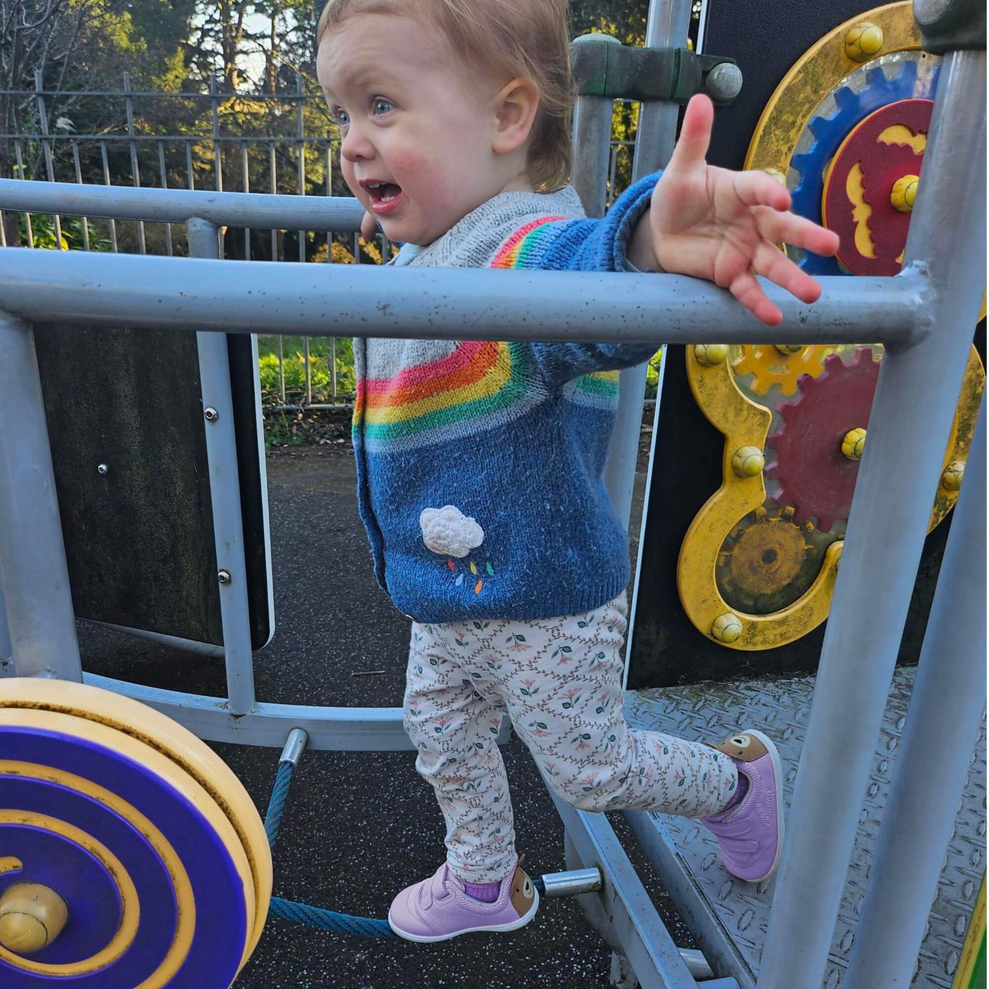 Kid wearing lilac barefoot trainers with bear details on the heel playing on an outdoor climbing frame.
