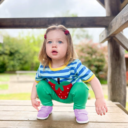 Kid crouching outdoors on a wooden platform wearing lilac barefoot trainers with hook-and-loop straps.