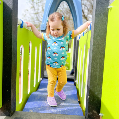 Kid wearing lilac barefoot trainers walking across a blue bridge on an outdoor playground.