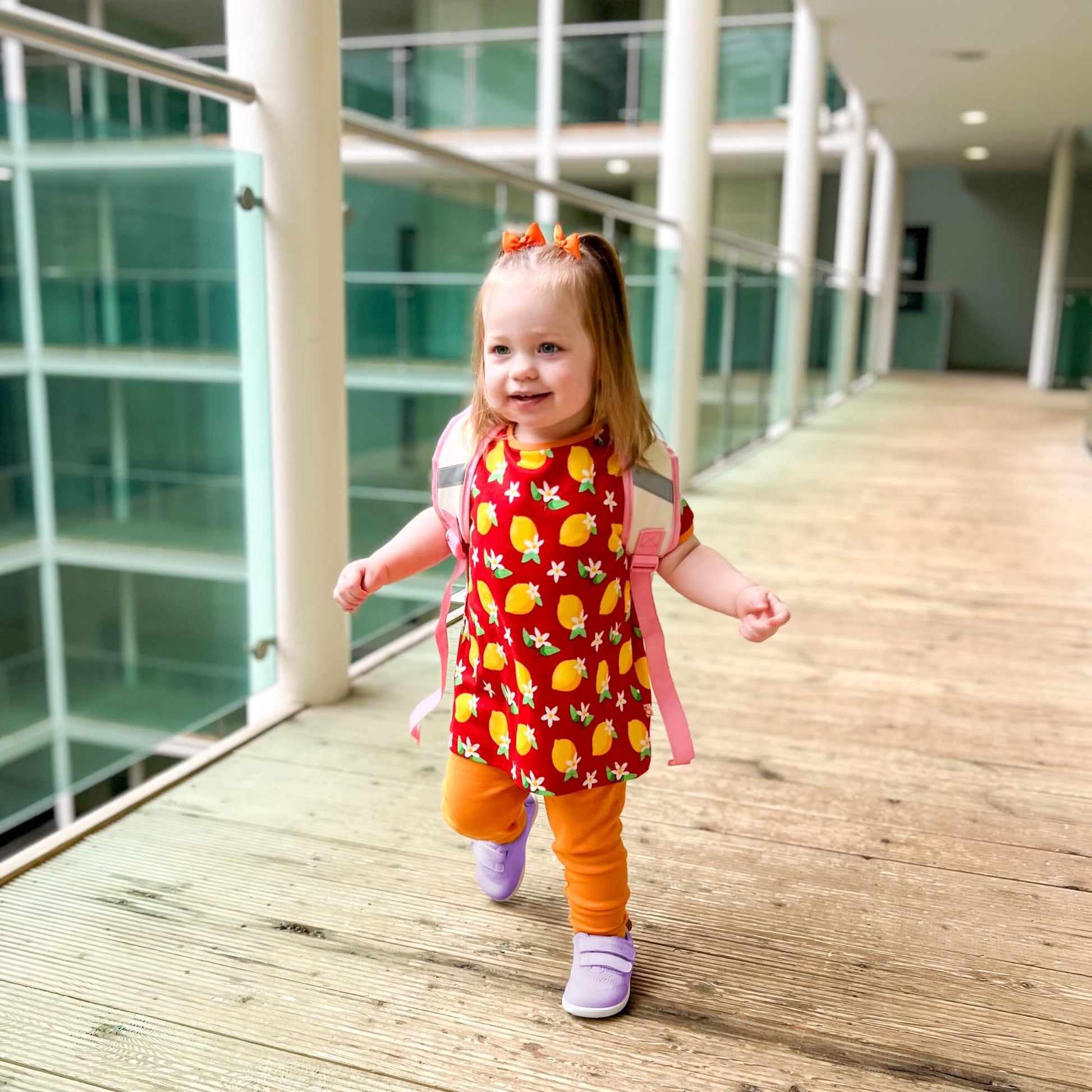 Kid wearing lilac barefoot trainers with hook-and-loop straps walking down an indoor wooden corridor.