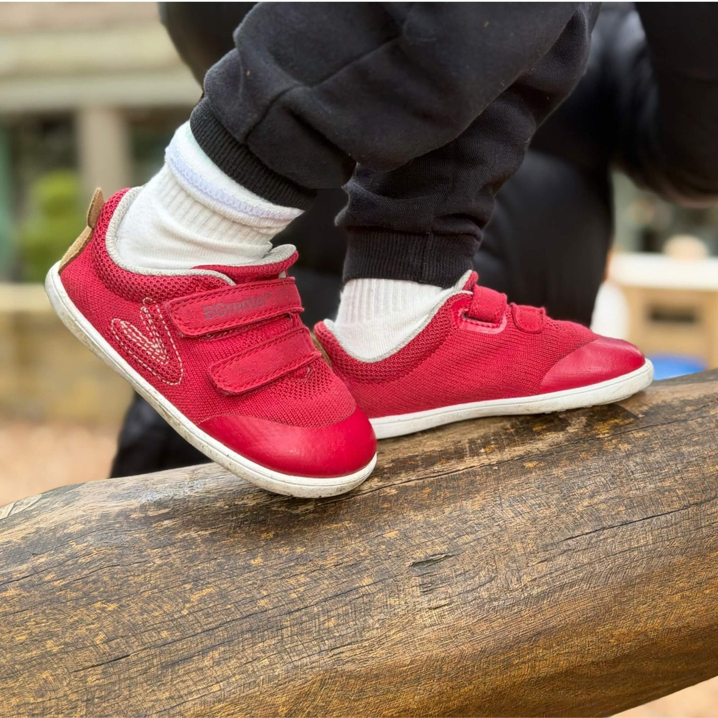 Kid's red barefoot trainers on an outdoor wooden log.