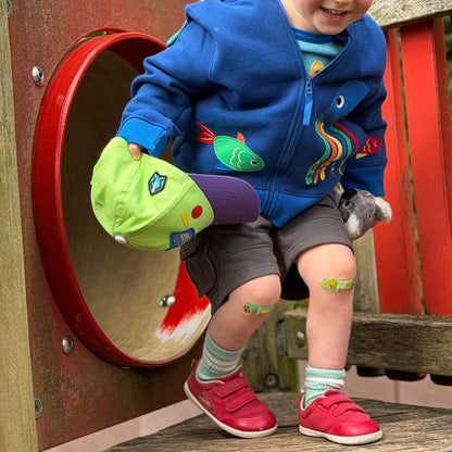 Kid wearing red barefoot trainers next to an outdoor playground tunnel.