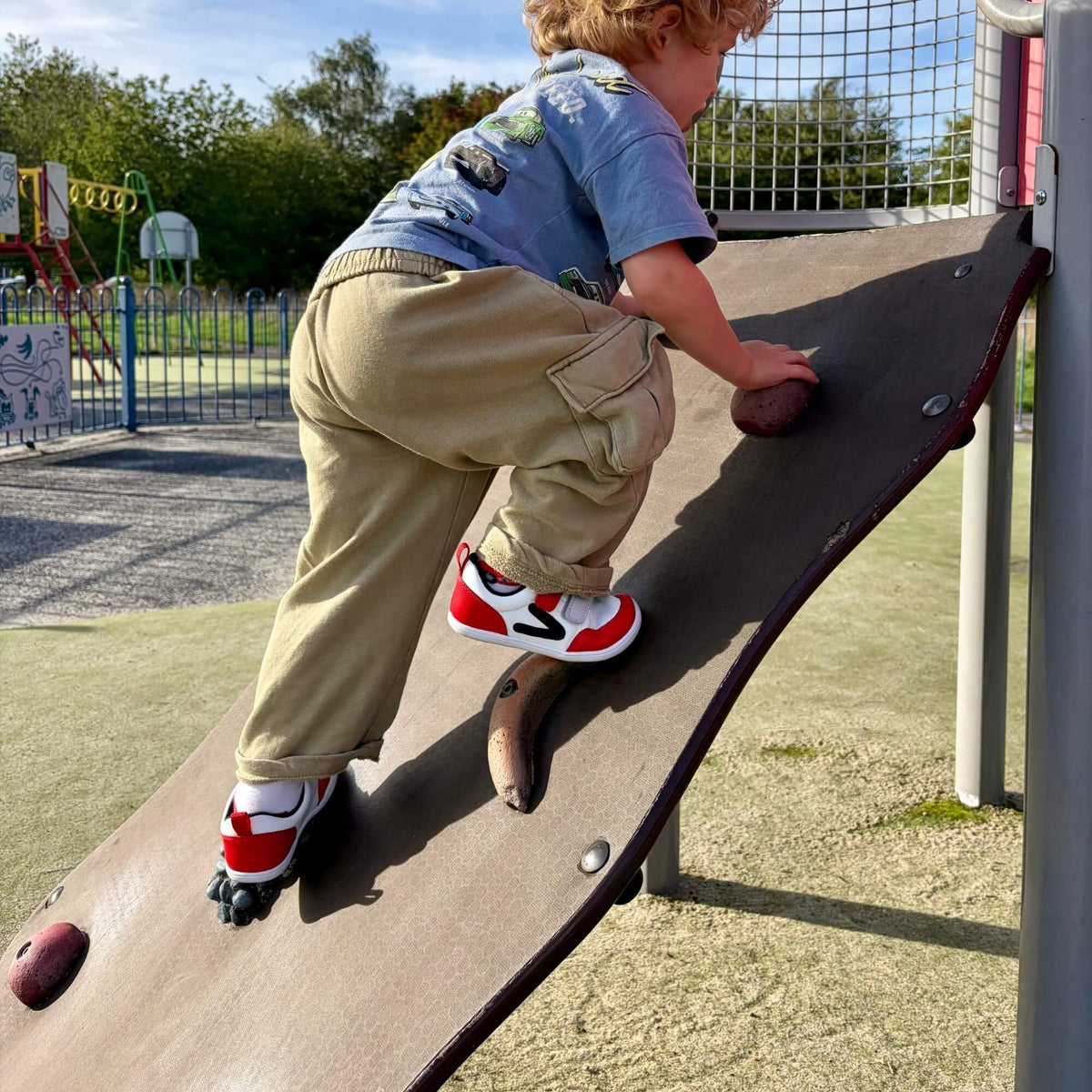 Kid wearing red and white leather barefoot trainers outdoors.