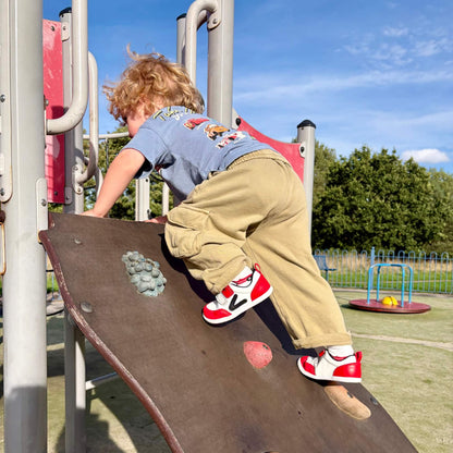 Kid's red and white leather barefoot trainers with flexible soles on an outdoor climbing frame.