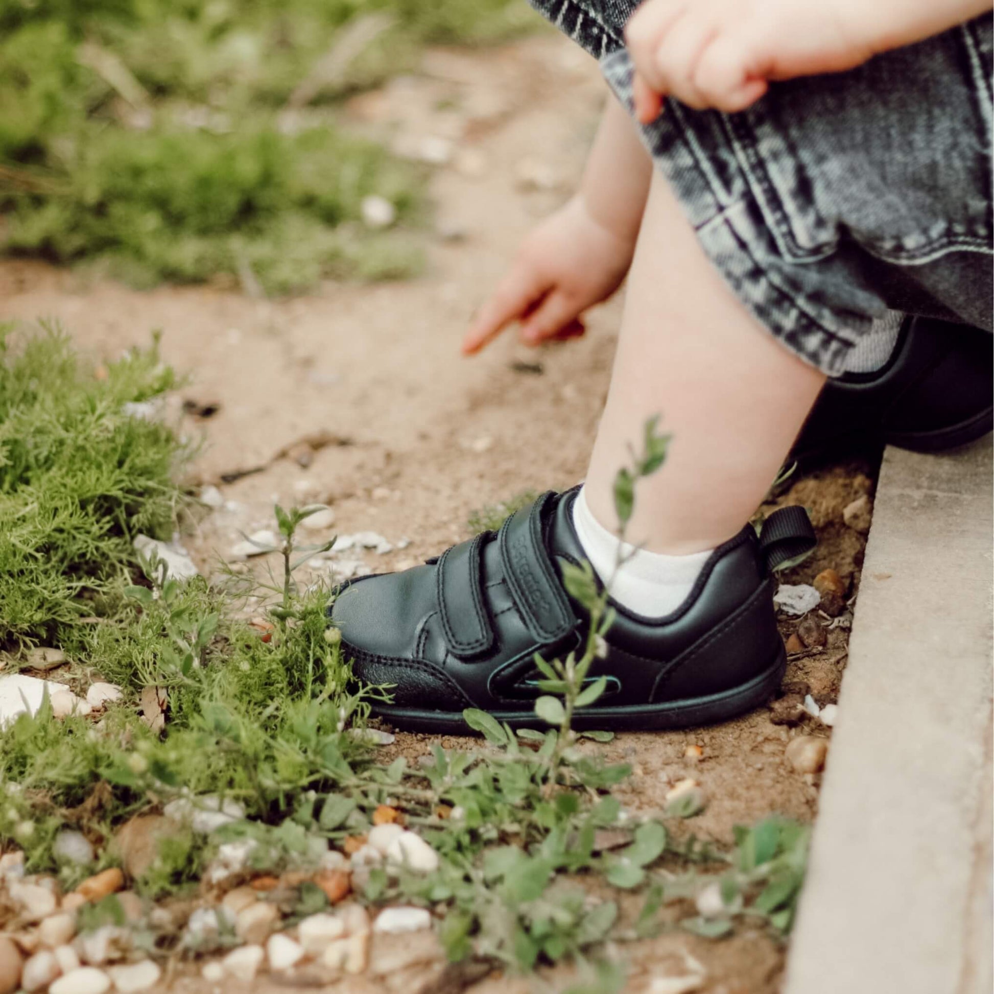 Toddler wearing black barefoot trainers sitting in park close up of shoes.