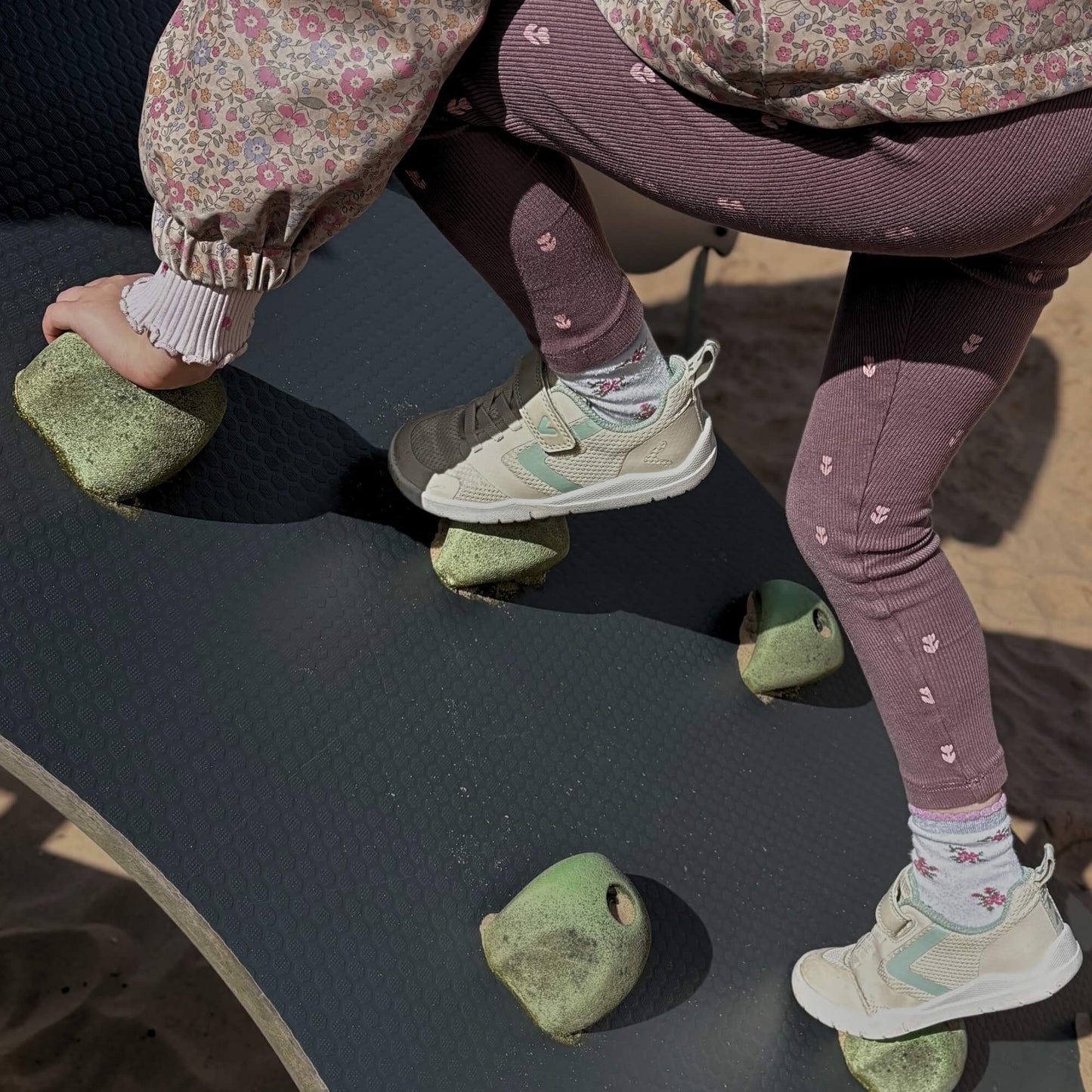 A kid wearing light beige barefoot trainers climbing an outdoor playground structure.