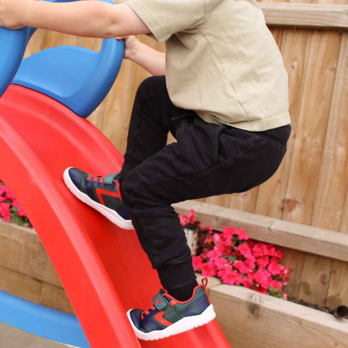Kid wearing green and navy barefoot trainers climbing up an outdoor playground slide.