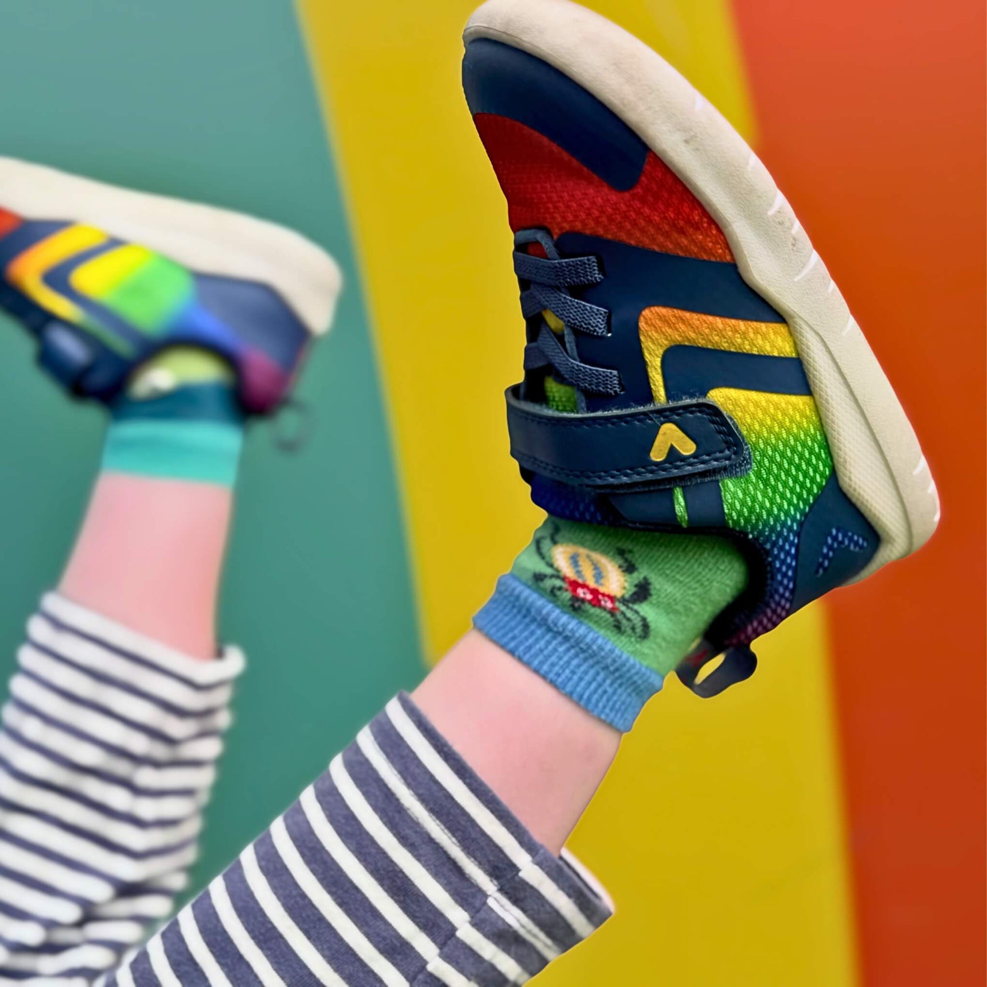 Close up of rainbow coloured trainers with rainbow wall in background