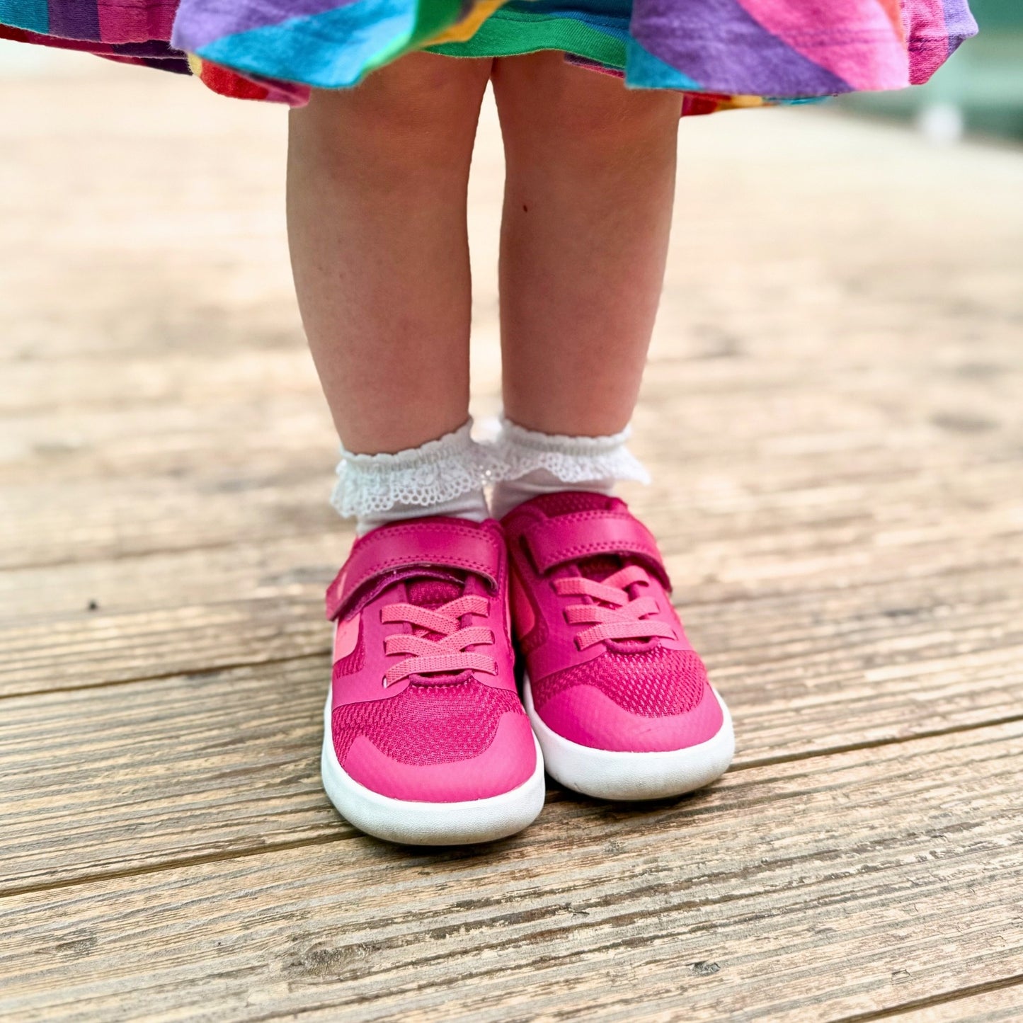 Girl wearing pink barefoot trainers standing in rainbow skirt