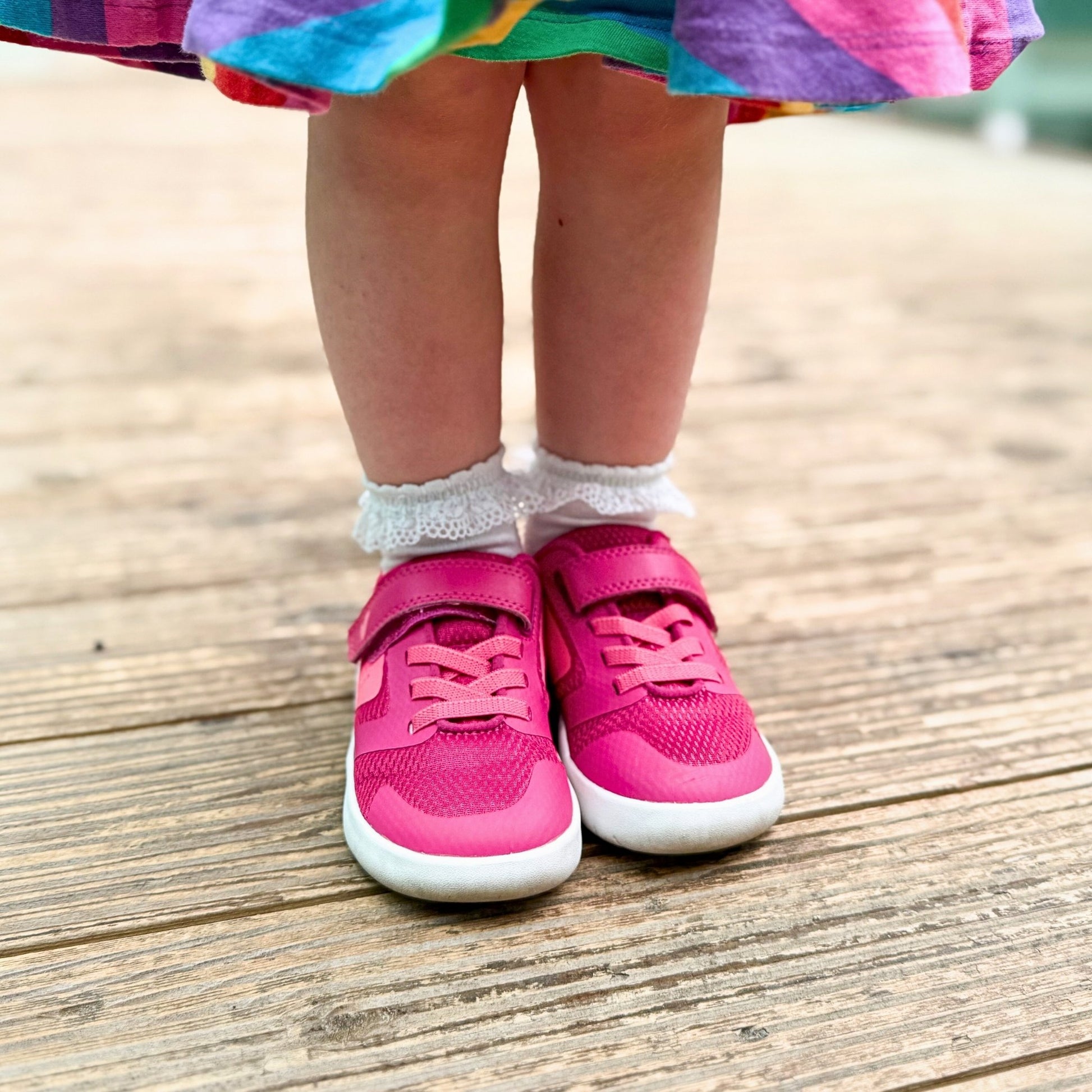 Girl wearing pink barefoot trainers standing in rainbow skirt