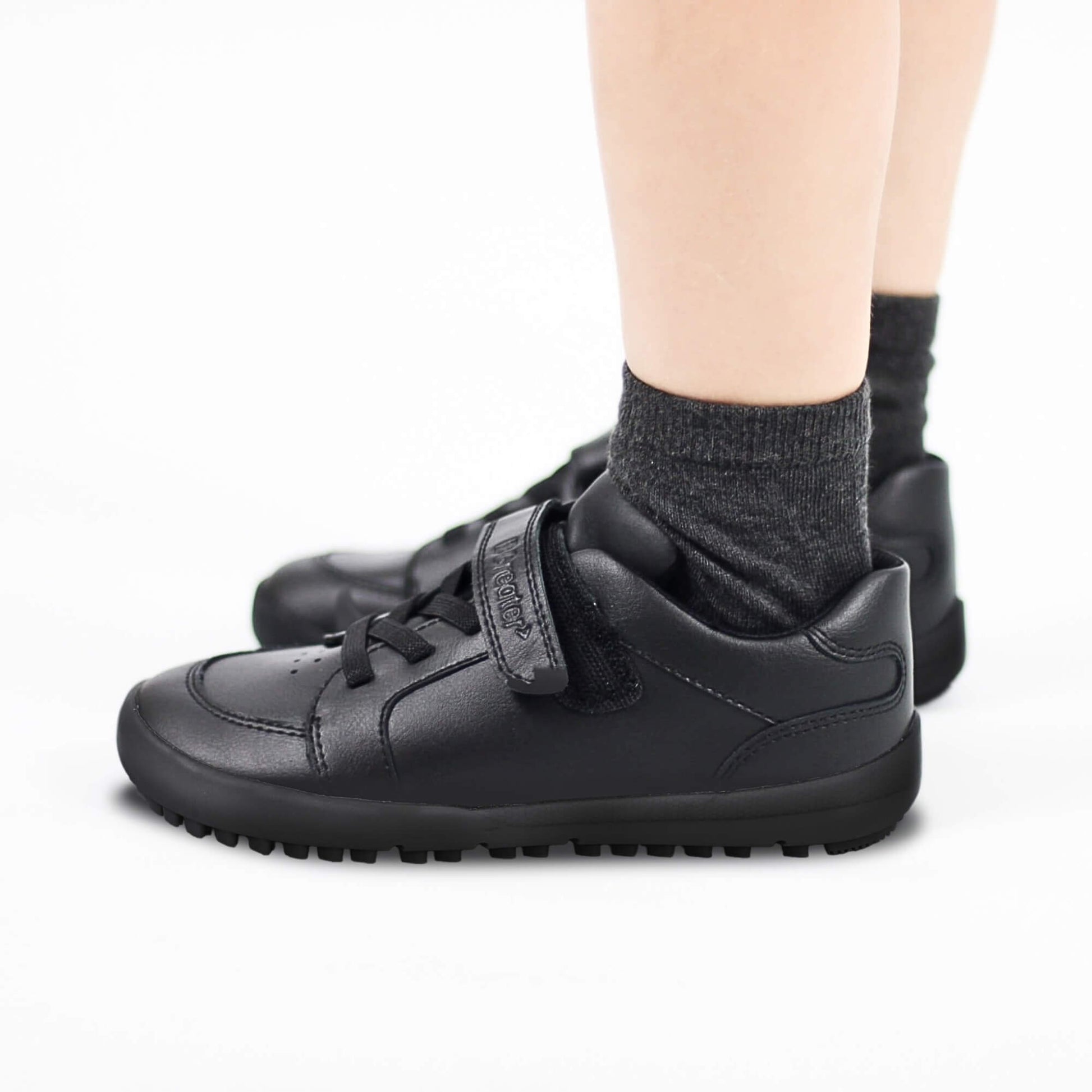 Black sneakers with velcro straps worn by a boy on a white background