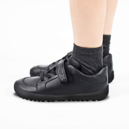 Black sneakers with velcro straps worn by a boy on a white background