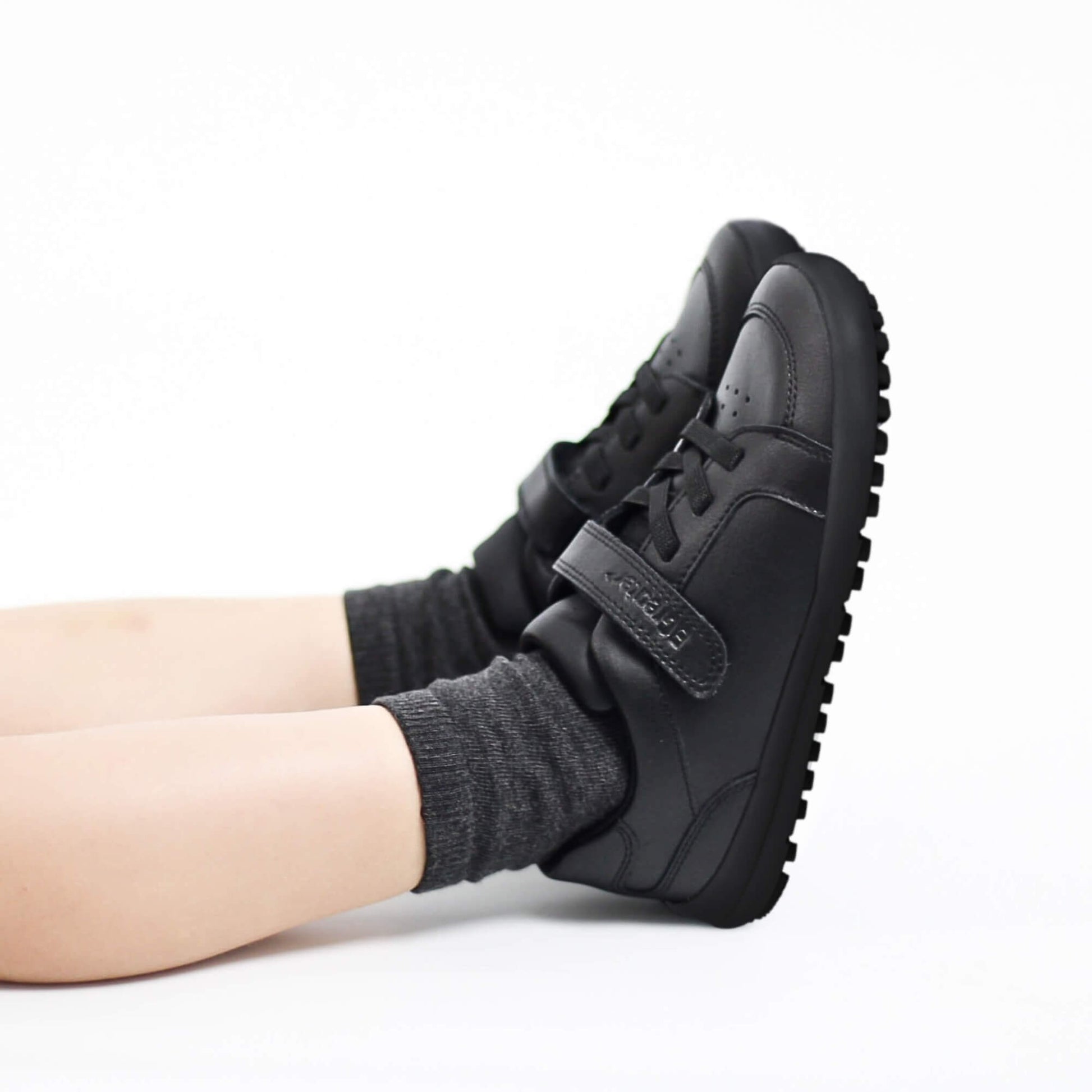 Black sneakers with velcro straps worn by a boy on a white background
