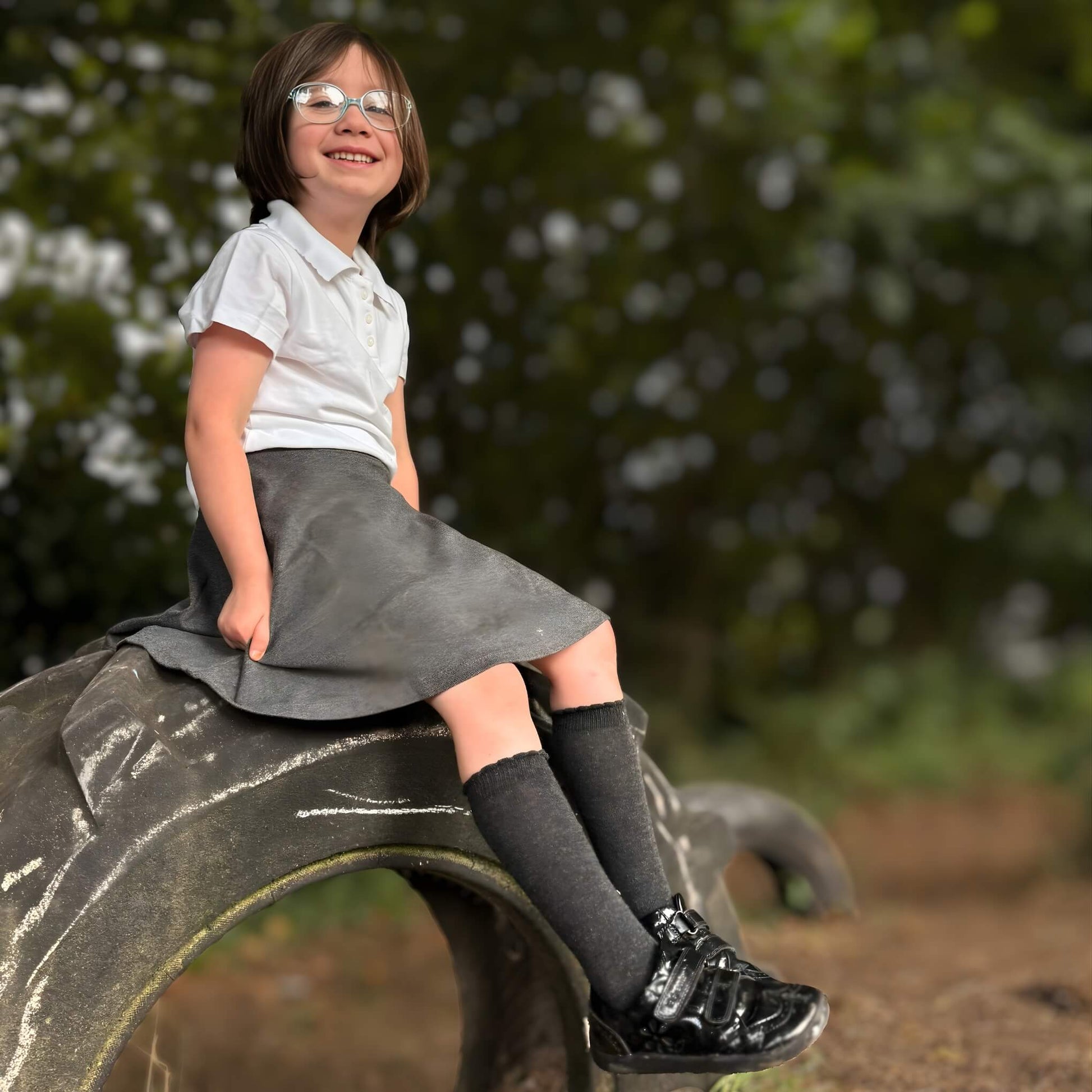 Girl sitting on tyre wearing closed girls school shoes in forest