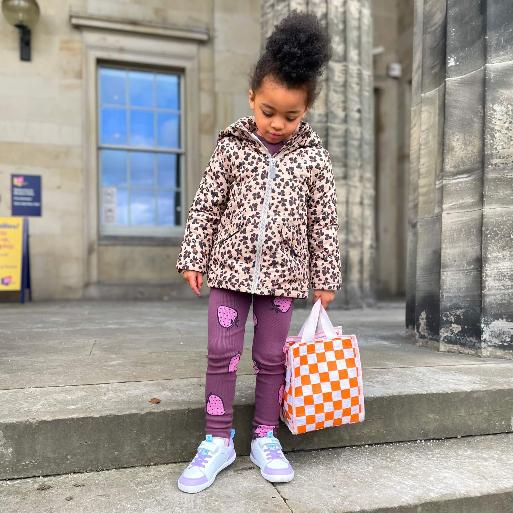 Kid wearing white and lilac leather barefoot trainers standing on outdoor stone steps.