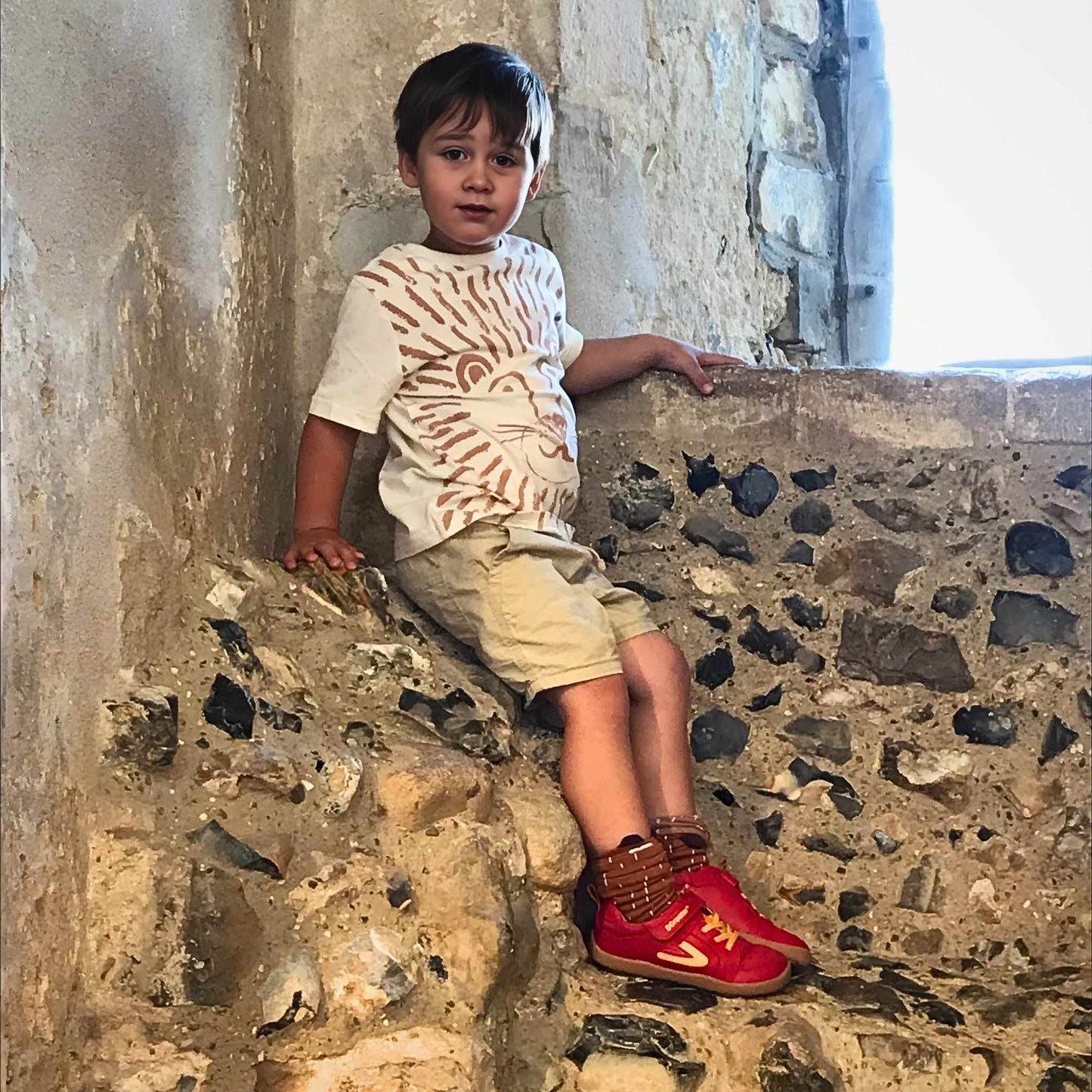 Child sitting on a stone wall wearing red barefoot trainers.