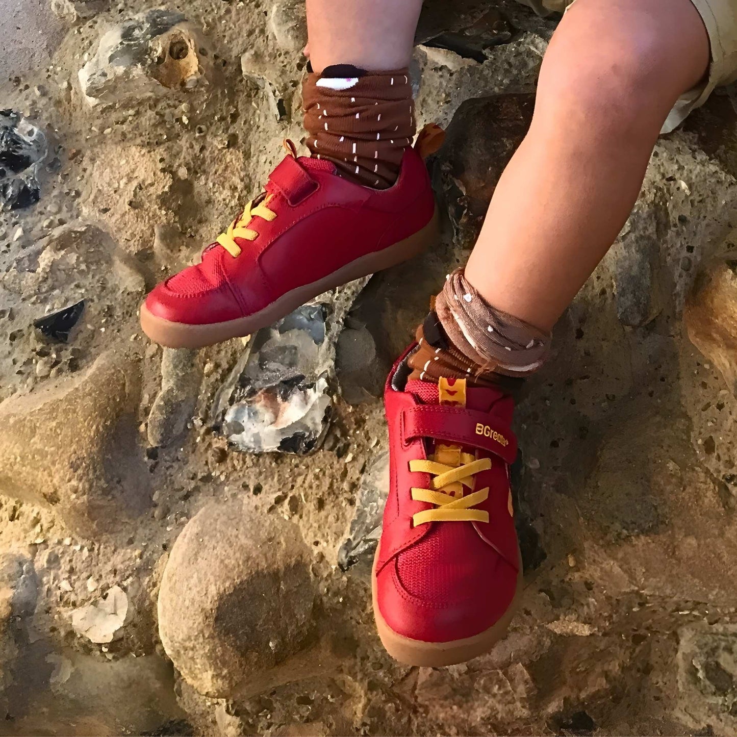 Child sitting on a stone wall wearing red barefoot trainers closeup