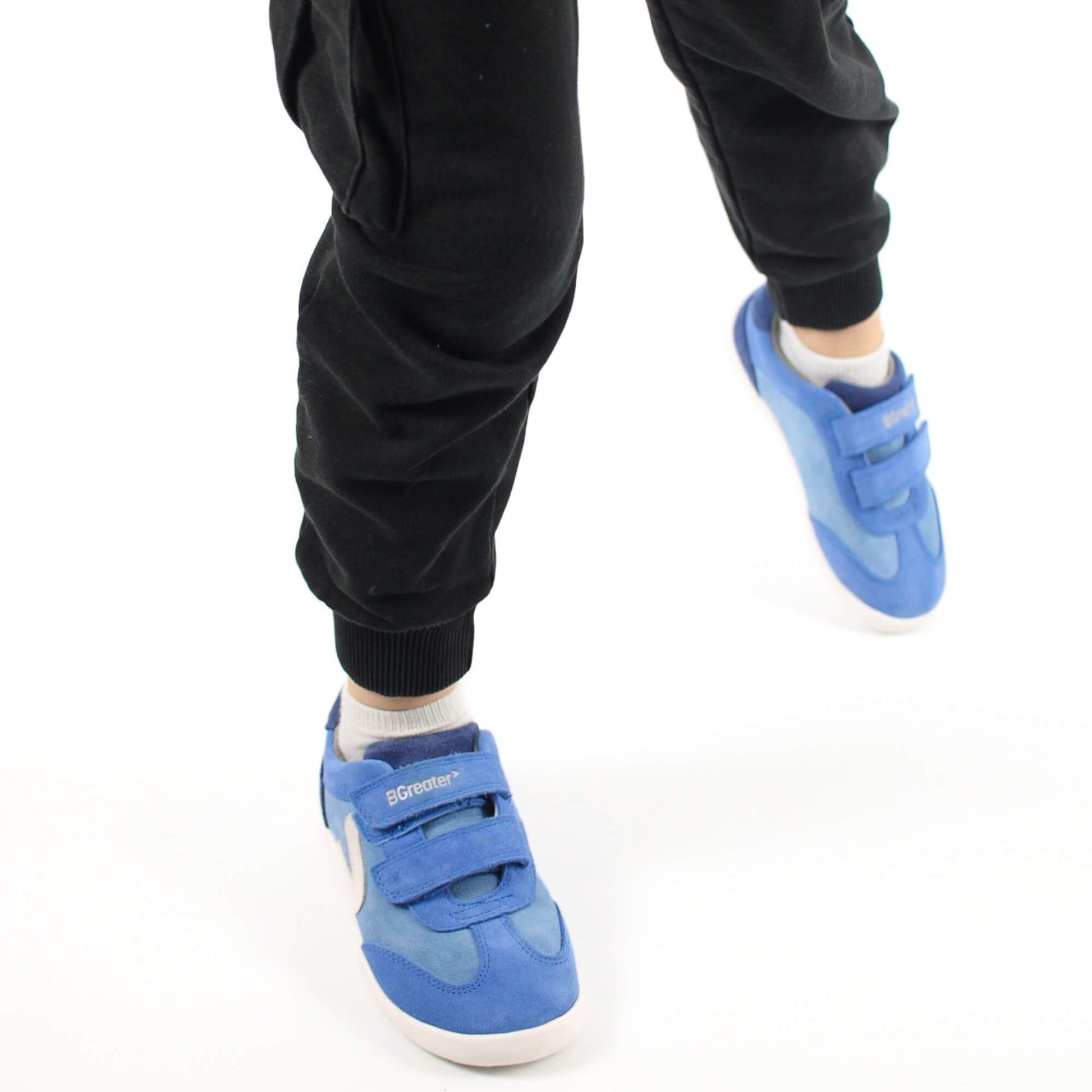 A close-up view of a kid taking a step in blue leather barefoot trainers against a white studio background.