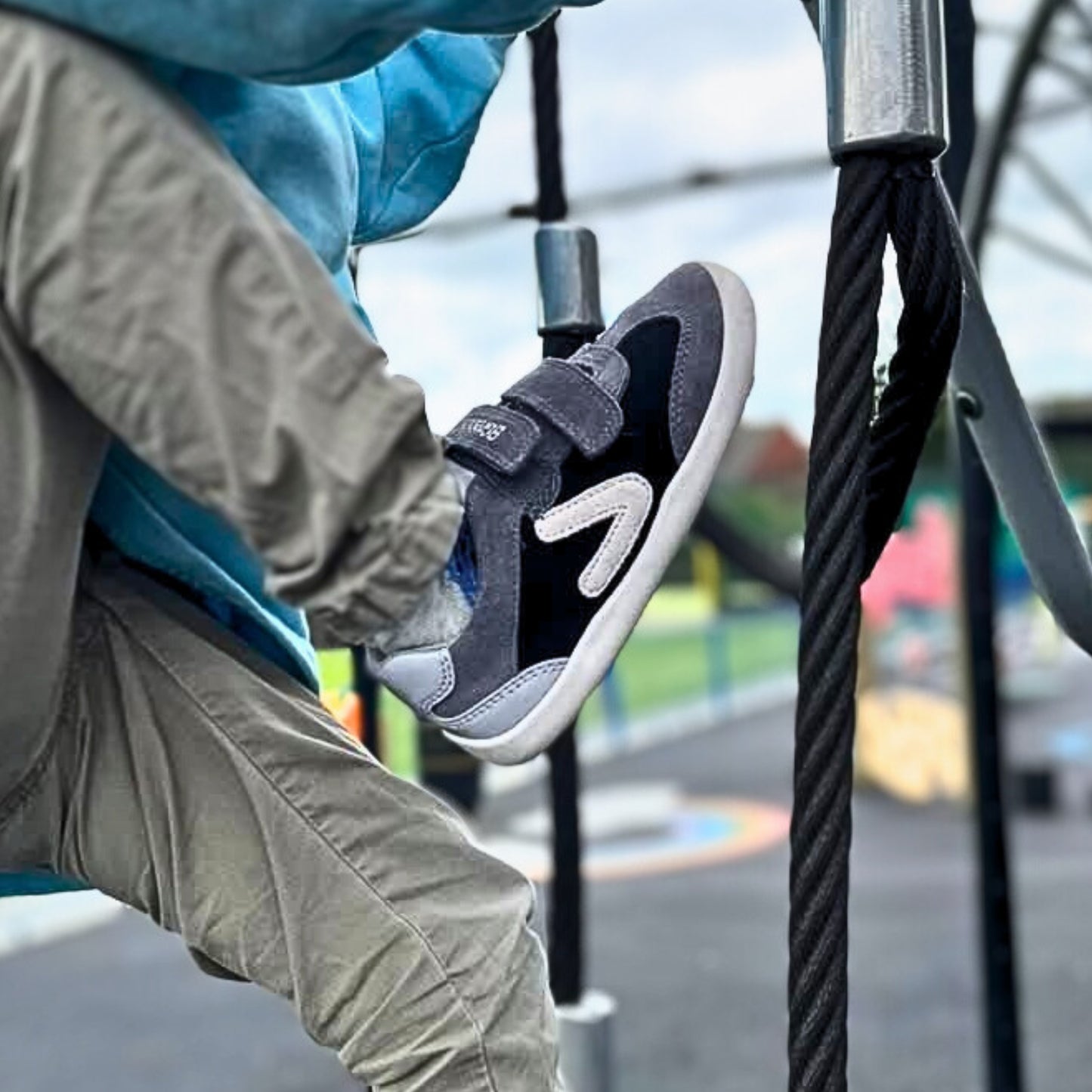 Boy climbing on rope ladder wearing black barefoot trainers.