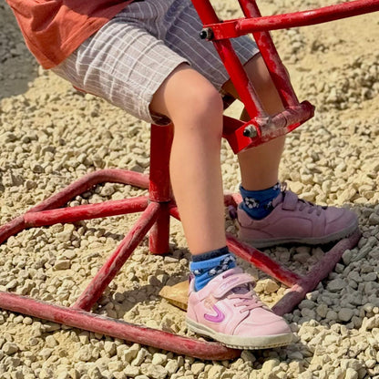 Kid's pink barefoot trainers on an outdoor playground structure over gravel.
