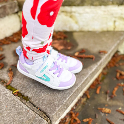 Close-up of kids white and lilac leather barefoot trainers on outdoor stone steps.