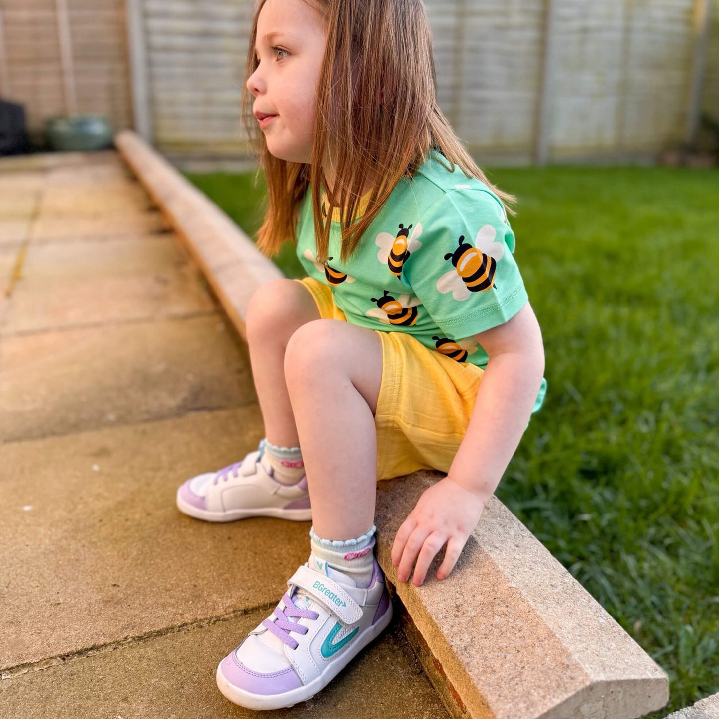 Kids white and lilac leather barefoot trainers with flexible soles pictured outdoors.