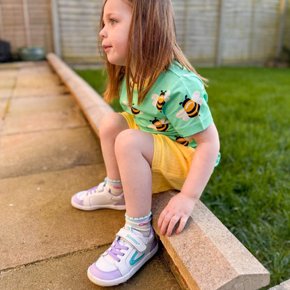 Kids white and lilac leather barefoot trainers with flexible soles pictured outdoors.