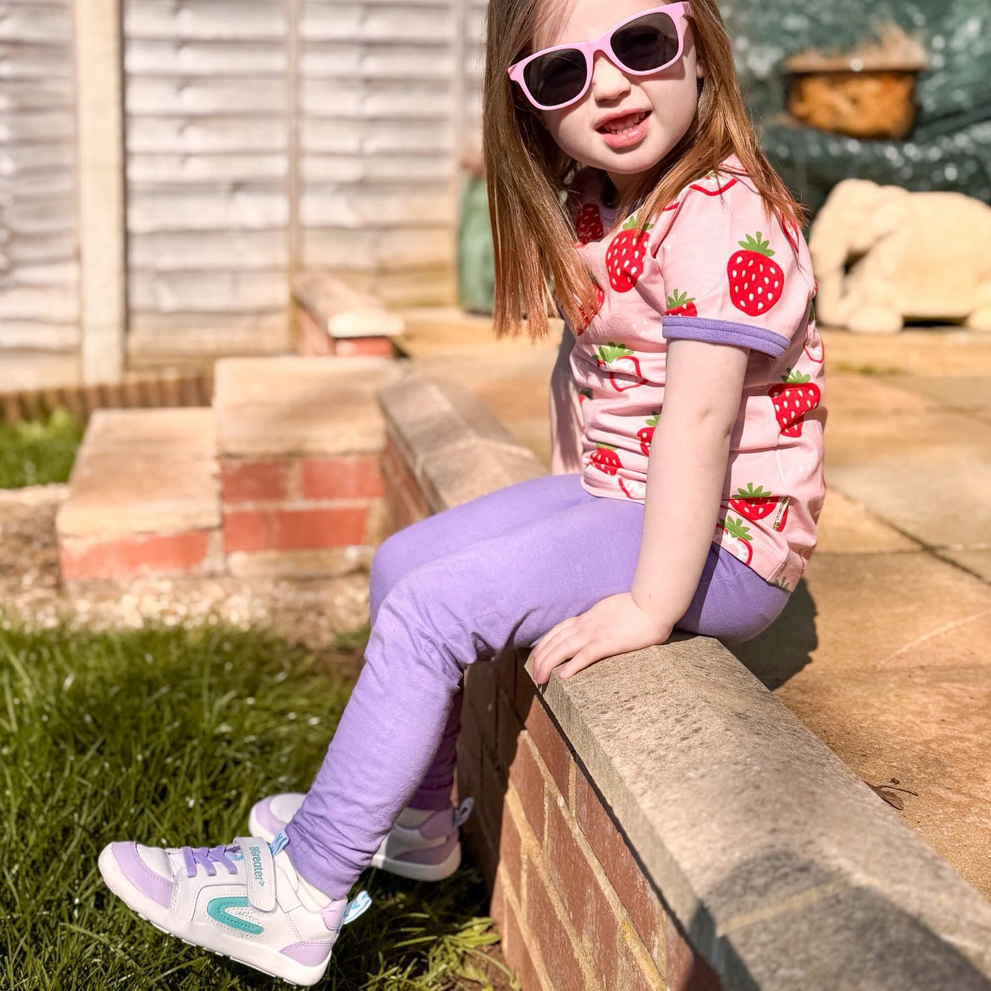 Kid wearing white and lilac leather barefoot trainers in an outdoor garden.