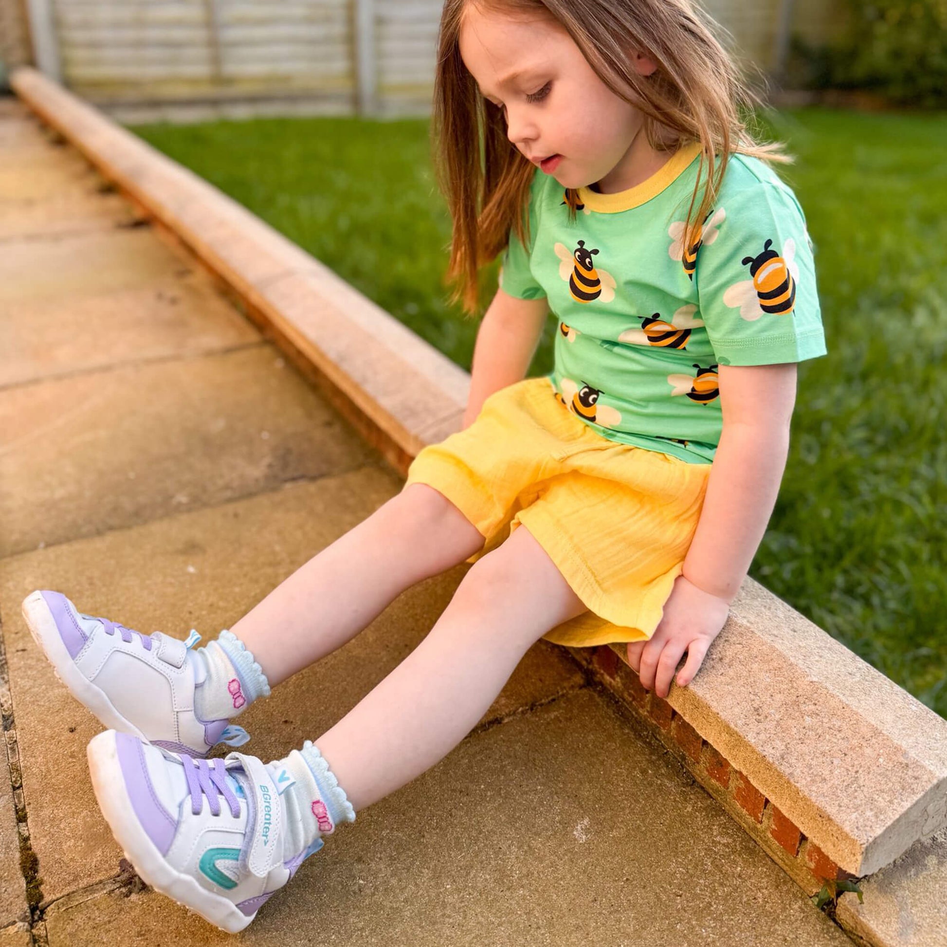 Kids white and lilac leather barefoot trainers on an outdoor patio.
