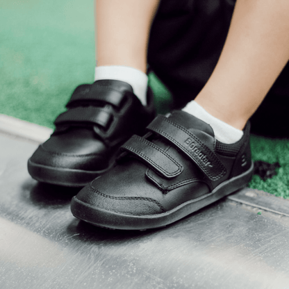 Close-up view of boys' black leather barefoot school shoes with double hook-and-loop straps outdoors.