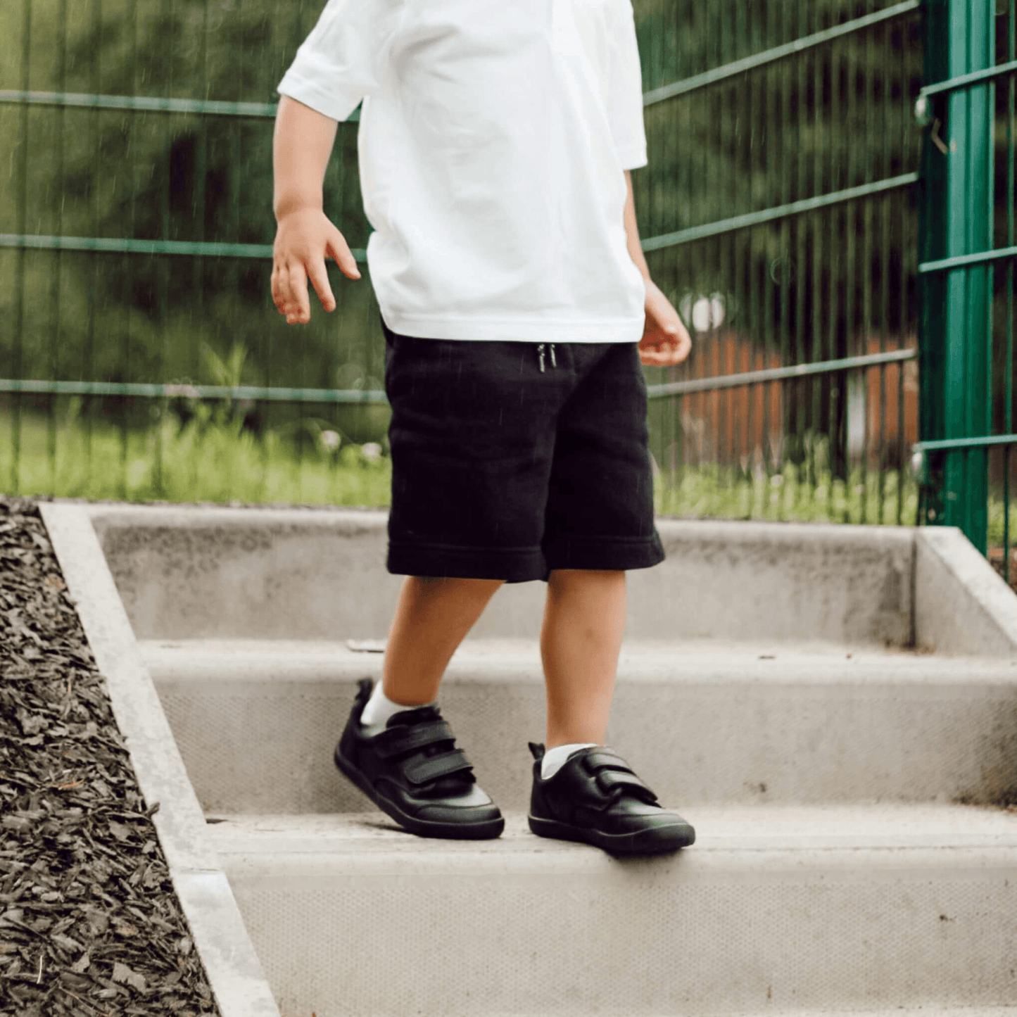 Boy wearing black leather barefoot school shoes walking down outdoor concrete steps.