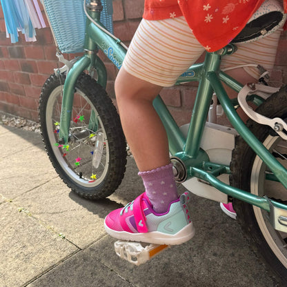 Kid's pink and teal barefoot trainers on a bike pedal outdoors.