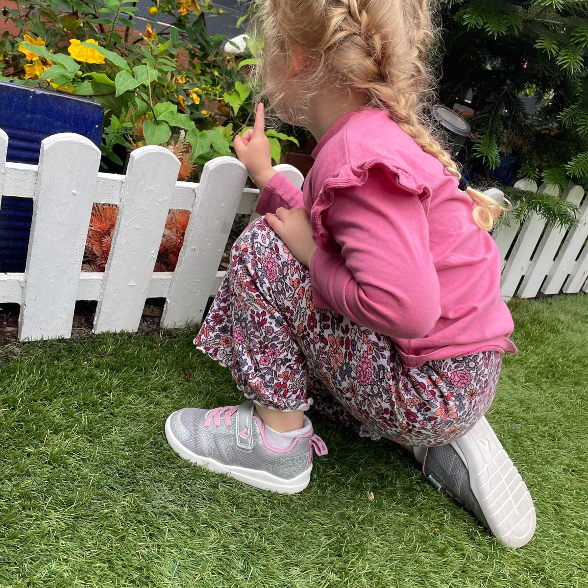 Kid crouching outdoors in silver and pink barefoot trainers showing flexible soles.